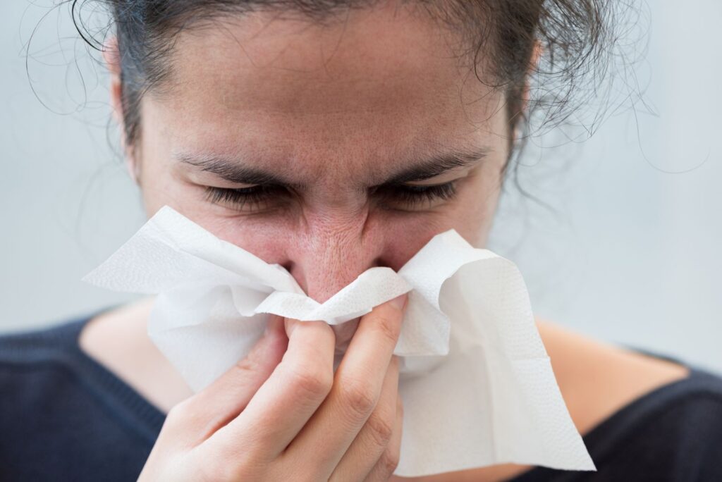 Woman experiencing nasal congestion blowing her nose on a tissue