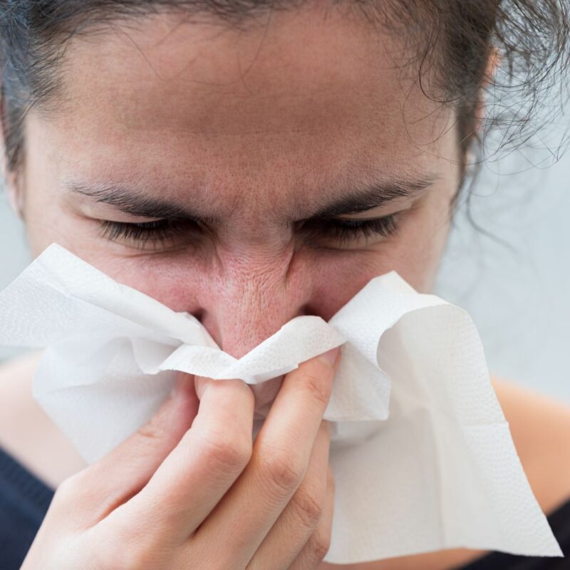 Woman experiencing nasal congestion blowing her nose on a tissue