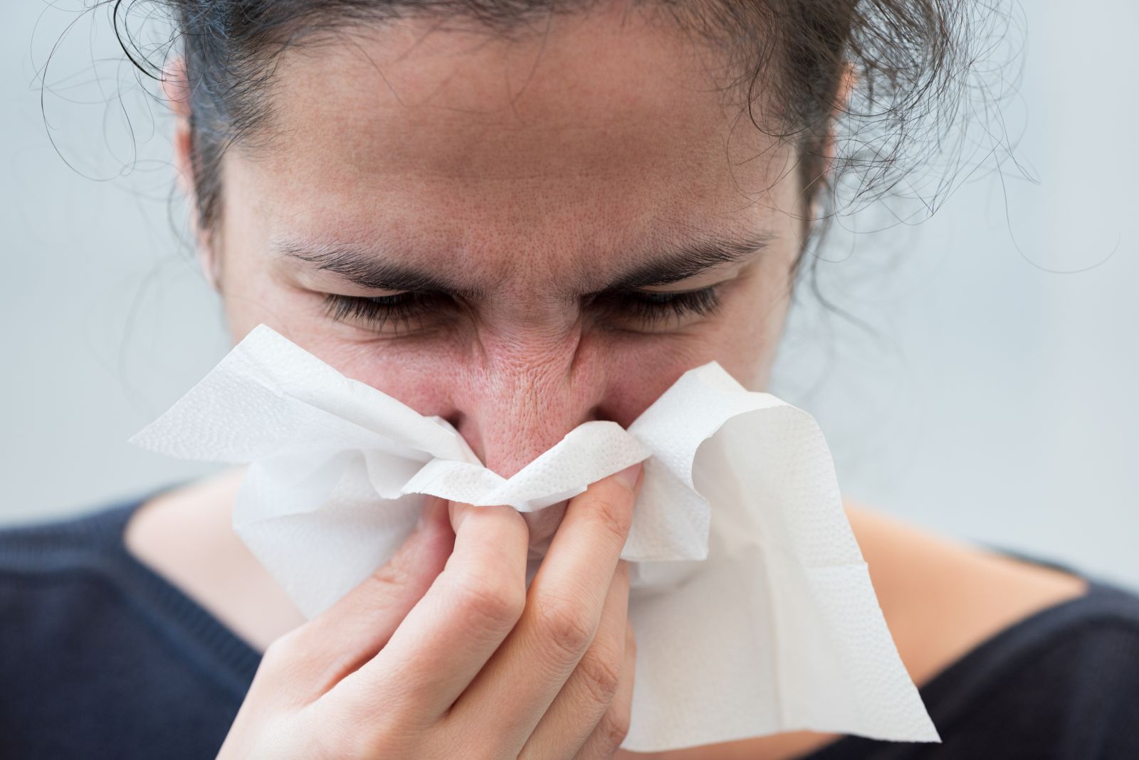 Woman experiencing nasal congestion blowing her nose on a tissue